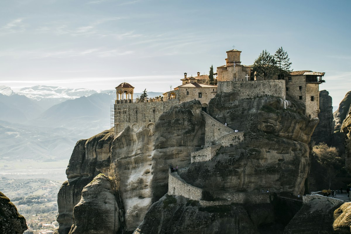 A Meteora monastery on top of a sandstone pillar with mountains behind