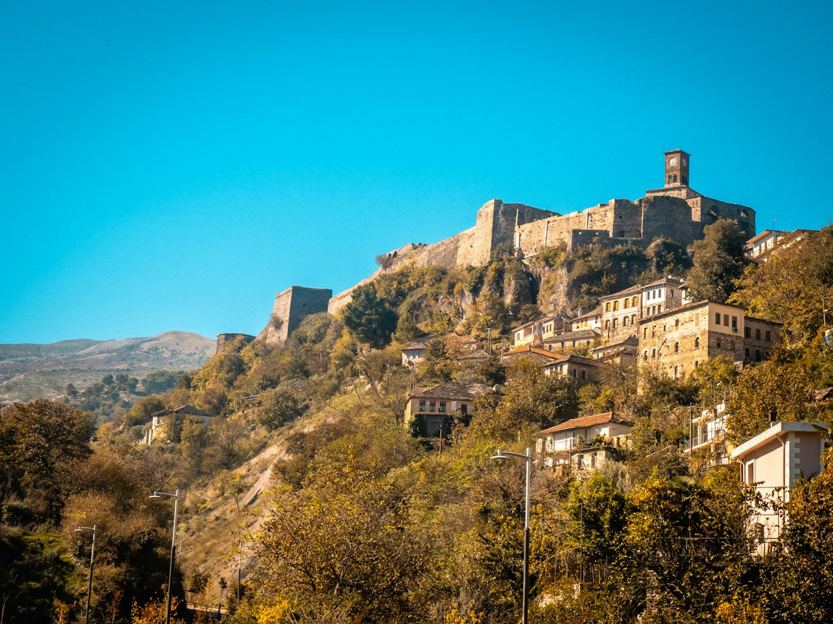 Stone houses and a castle with a clock tower on a hillside above Gjirokastra
