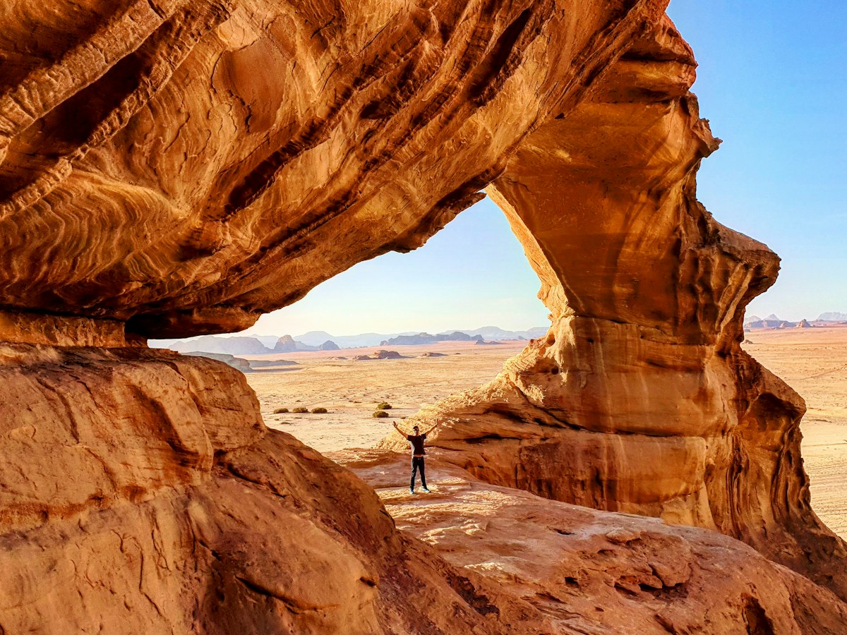A traveller standing under a natural sandstone arch looking out over open desert